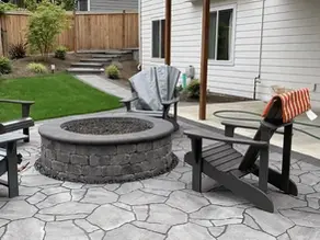 Backyard paver patio featuring a built-in circular fire pit surrounded by Adirondack chairs and landscaped lawn.