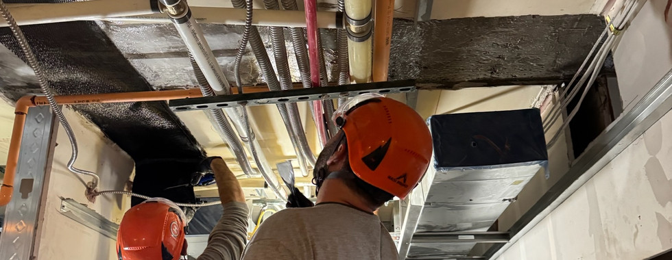 Construction crew installing carbon fiber reinforcement around existing mechanical lines in a confined slab opening.
