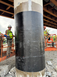 Two workers standing near a finished carbon fiber–wrapped column during final inspection.