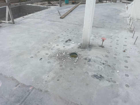 Pre-repair condition of a post-tensioned concrete slab showing drilled holes and surface preparation for reinforcement. Structural markings indicate planned areas for additional strengthening