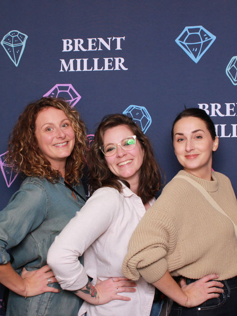 3 girls standing in front of a step and repeat banner with Brent Miller's logo and some hand-drawn diamonds, each girl has a hand on their hip and posing for Ziggy Booth's Traditional Booth