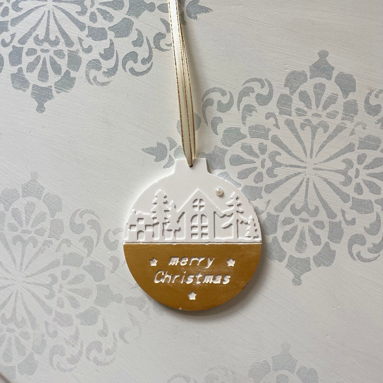 Julekugle i hvid stengips med gyldne detaljer og stemplet “Merry Christmas”.