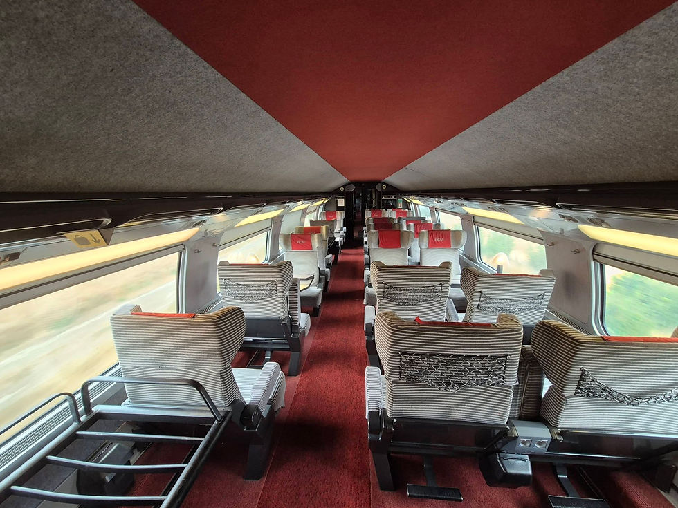 Empty modern SNCF TGV first class train carriage with striped seats, red carpet, and blurred scenery outside; red headrests.