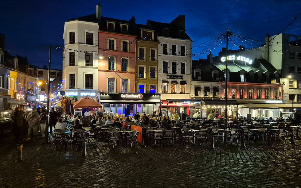 Night time cobblestone square in Boulogne sur Mer France with colourful café buildings, string lights, and crowds dining outdoors under a deep blue sky.