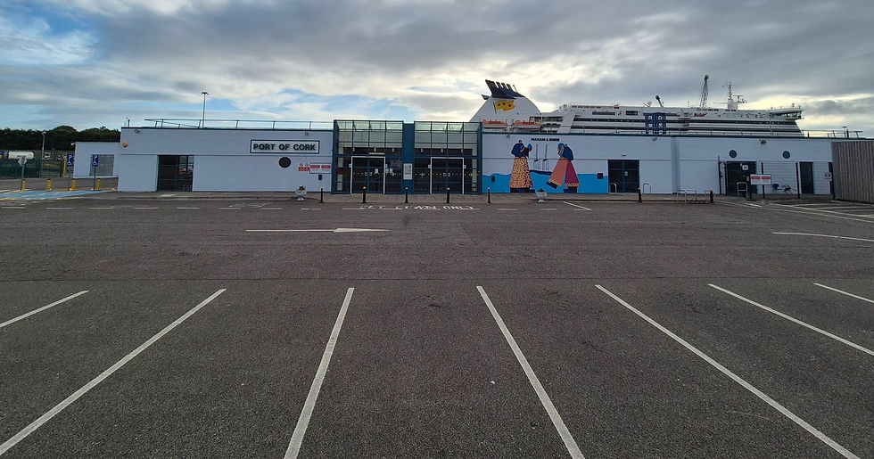 Empty Port of Cork ferry terminal with a large Hibernia Line ferry behind it under cloudy skies and a mural on the wall.