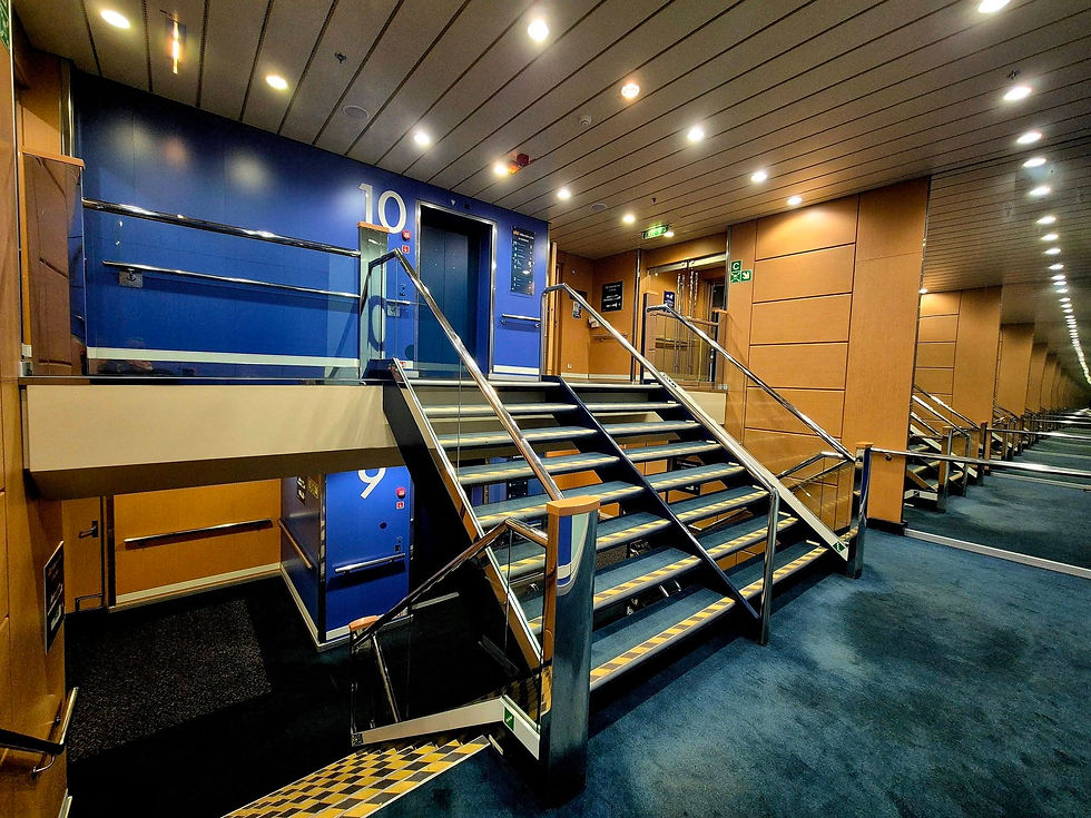 Empty Hibernia Line ship stairwell with blue deck doors labelled 9 and 10, metal railings, and warm overhead lights in a quiet interior.