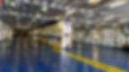 Empty ferry parking deck with shiny blue floor and yellow markings. Signs with numbers and instructions on pillars. Quiet atmosphere.