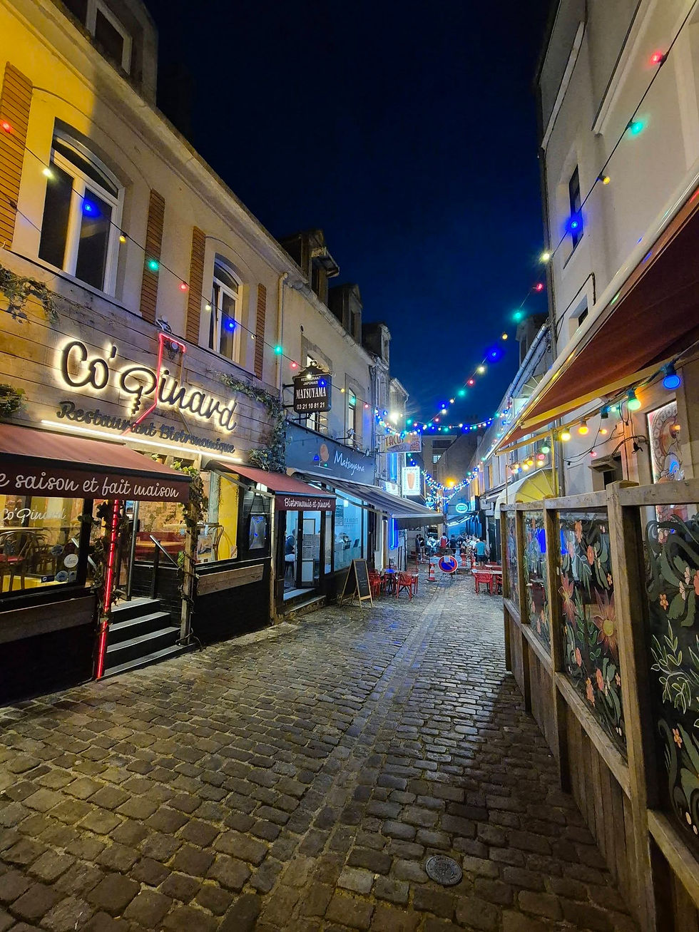 Night time cobblestone alley in Boulogne sur Mer France lined with restaurants and colourful string lights, with a few people gathered in the distance.