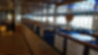 Spacious dining area with empty tables and chairs on a Moby Lines ferry. Large windows, striped flooring, and a serene, well-lit atmosphere.