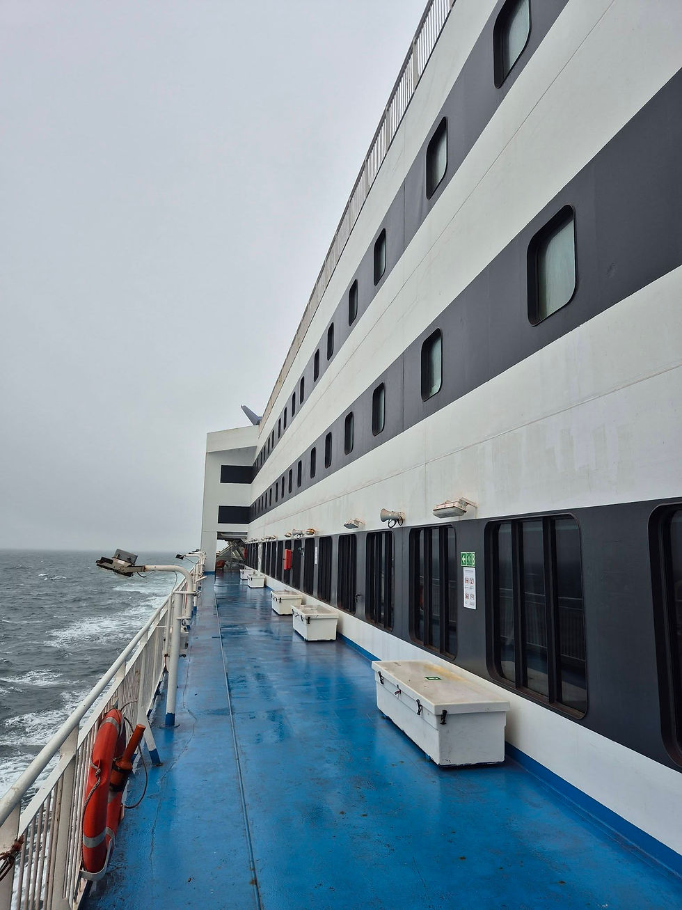 Empty Hibernia Line ferry deck beside grey Irish Sea, with a blue floor, white ship wall, dark windows, and an overcast sky.