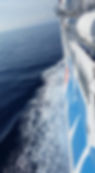 Moby Lines ferry Moby Corse sailing on a calm sea, view from the side with waves. Blue and white hull, lifeboats visible, clear sky above.