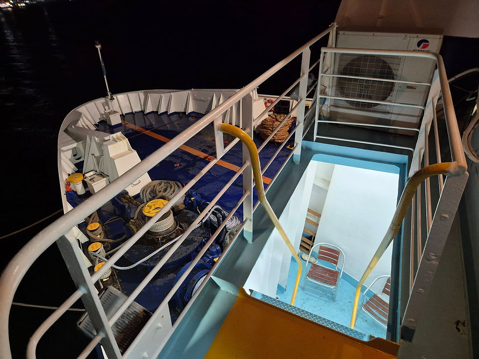 Ship deck at night, lit stairs leading below, ropes and equipment on blue floor, yellow railings, industrial setting, calm, no text visible.
