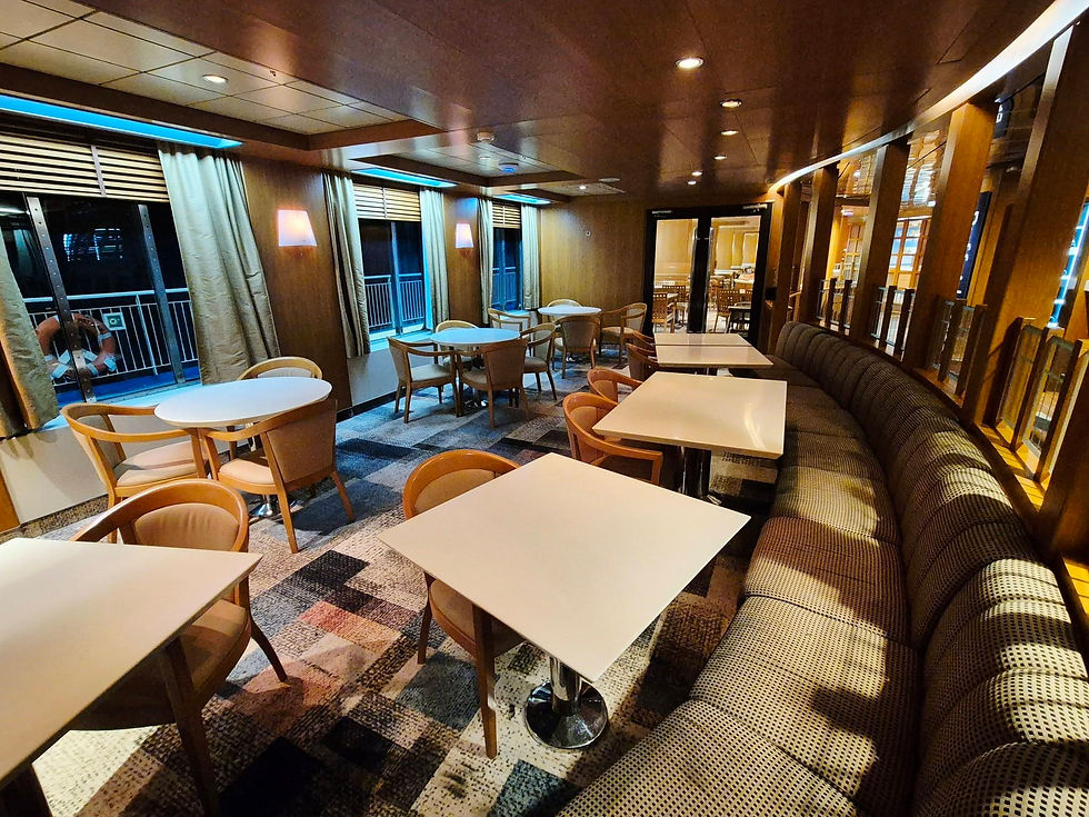 Empty Hibernia Line ship dining room with white tables, wooden chairs, curved bench seating, warm lighting, and windows overlooking the deck at night