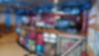 Pizzeria counter with colorful decor, resembling stacked crates and pipes. Sign reads "ACME Pizzeria." Bright, inviting atmosphere.