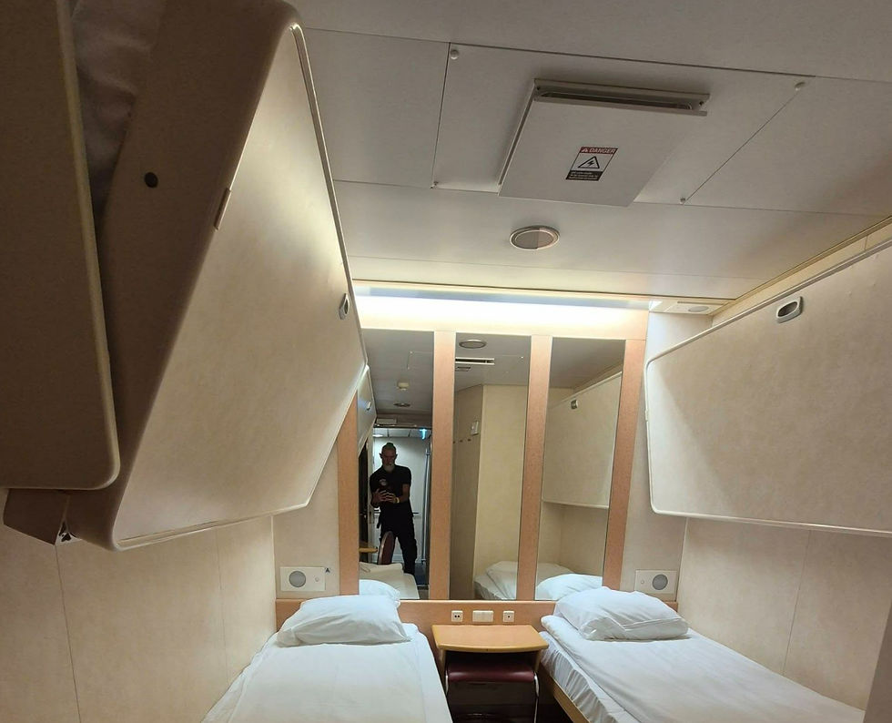 Four berth inside cabin with two single beds and mirror on Hibernia Line ferry; a man takes a selfie in the hallway, with a danger sign on the ceiling.