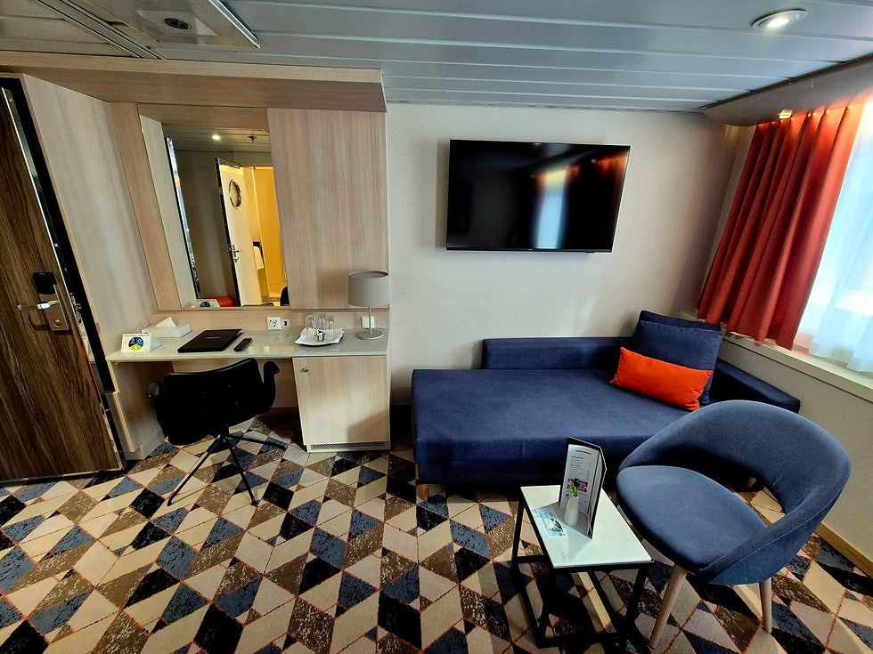 DFDS ship commodore cabin with blue sofa, desk, TV, red curtains, and patterned carpet; quiet, tidy, and empty