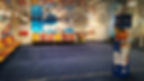 Colourful ferry lounge with empty orange and yellow seats. Cartoon murals and a costumed character. Blue carpet, restaurant sign on a pillar.