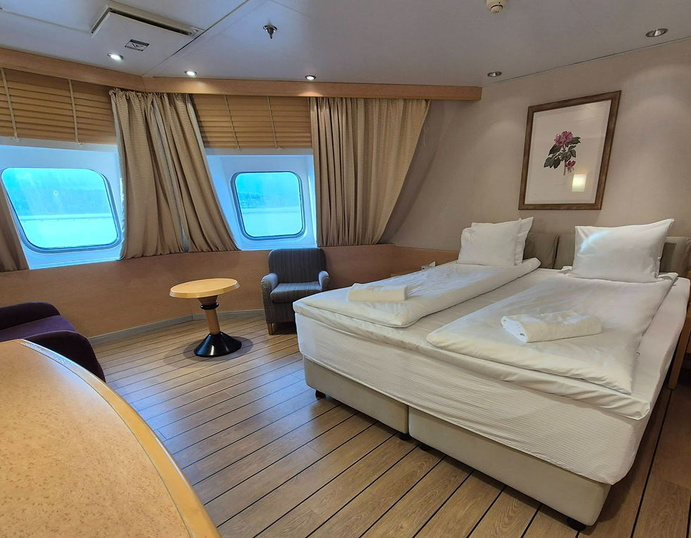 Cosy Hibernia Line ferry deluxe cabin with two twin beds, sea-view windows, beige curtains, small table and chairs, and framed flower art