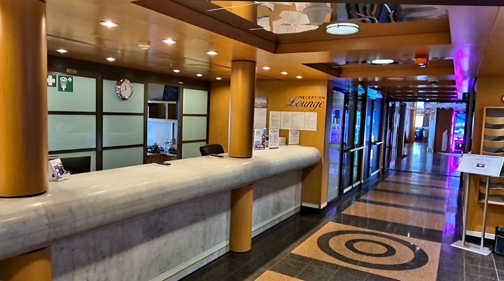 Empty Hibernia Line ferry reception desk with curved marble desk, warm wood panels, purple lights, and a spiral floor pattern.