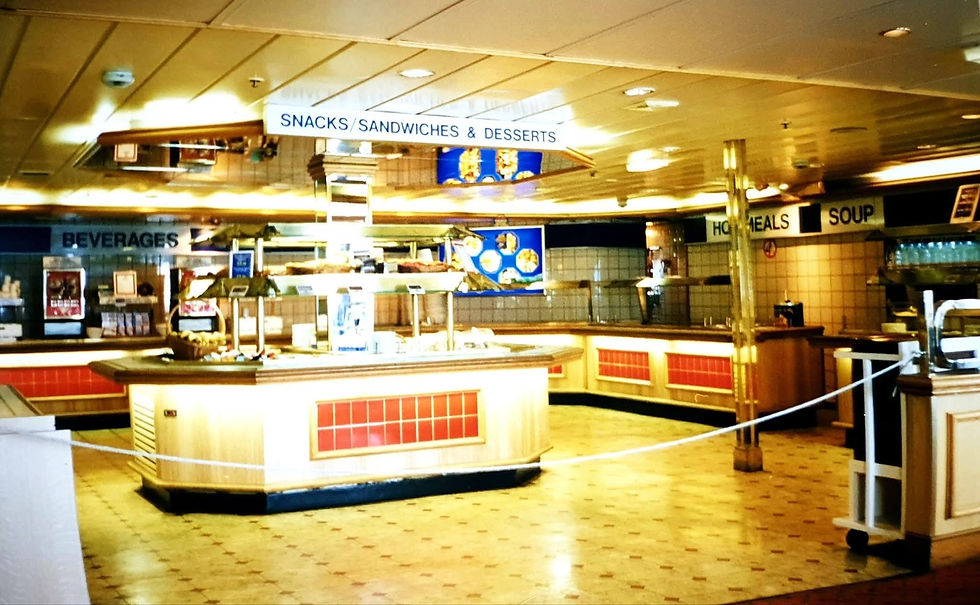 Empty cafeteria with tiled floors, red and white counters, signs for snacks, beverages, hot meals, and soup. Brightly lit and clean.