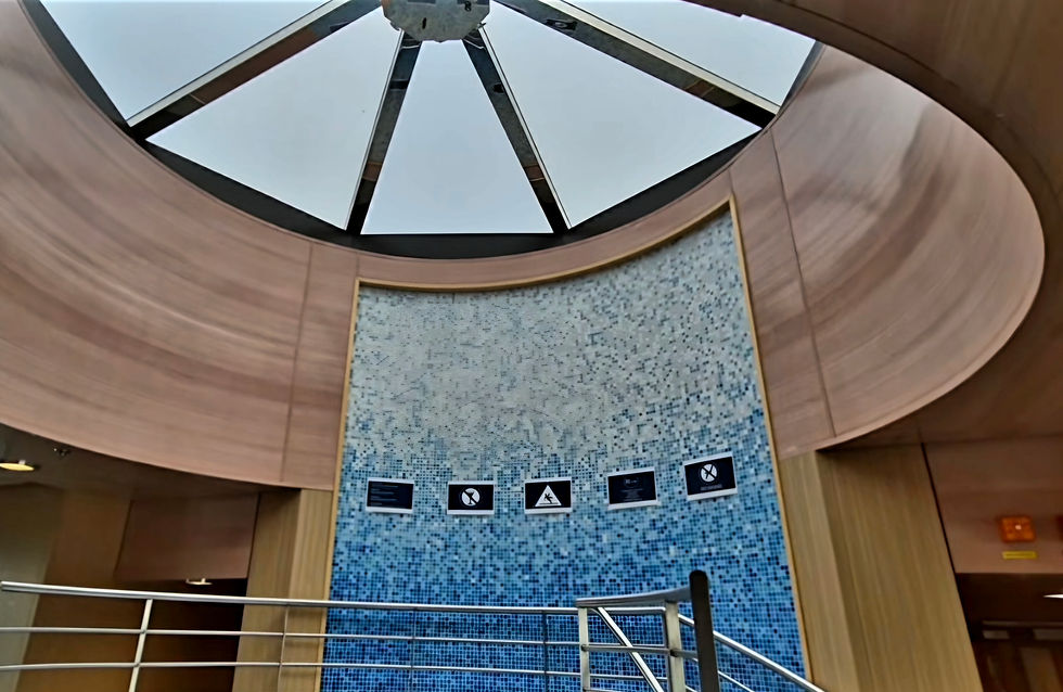Modern indoor spa aboard Hibernia Line ferry with a circular skylight, curved wood walls, blue mosaic mural, and metal railings below.