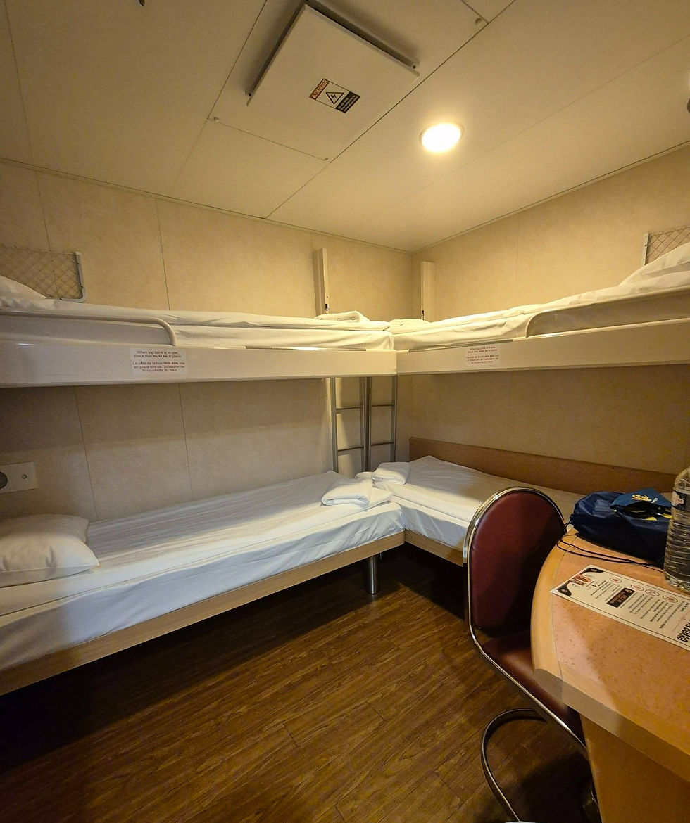 Warm-lit Hibernia Line ship cabin with two bunk beds, a small desk and chair, wood floor, and safety signs on beige walls.