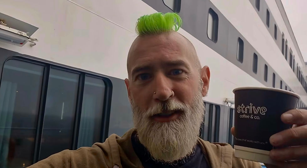 Man with neon green mohawk and beard holds a Strive Coffee cup on a Hibernia Line ship deck, looking into camera.