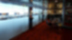 Modern cafe interior with red carpet, chrome chairs, and motorcycle photos. Frosted glass panels with text and figures in the background.
