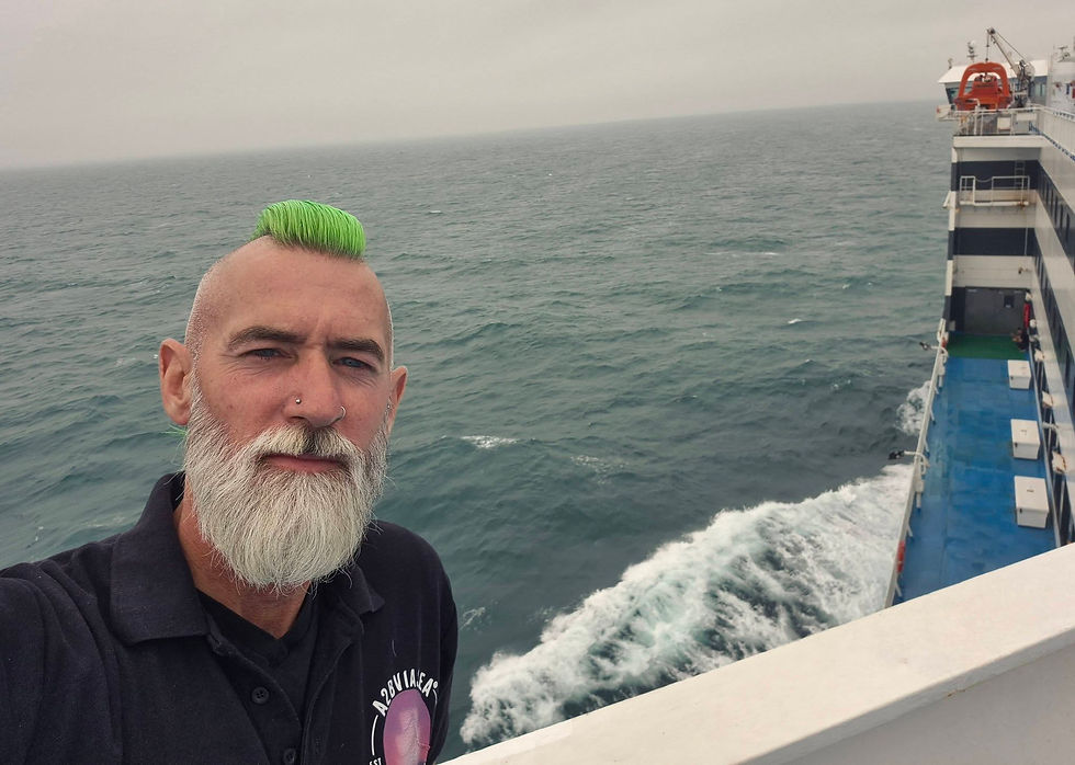 Selfie of a man with green mohawk and white beard on a Hibernia Line ship deck, with choppy sea and misty horizon behind him.