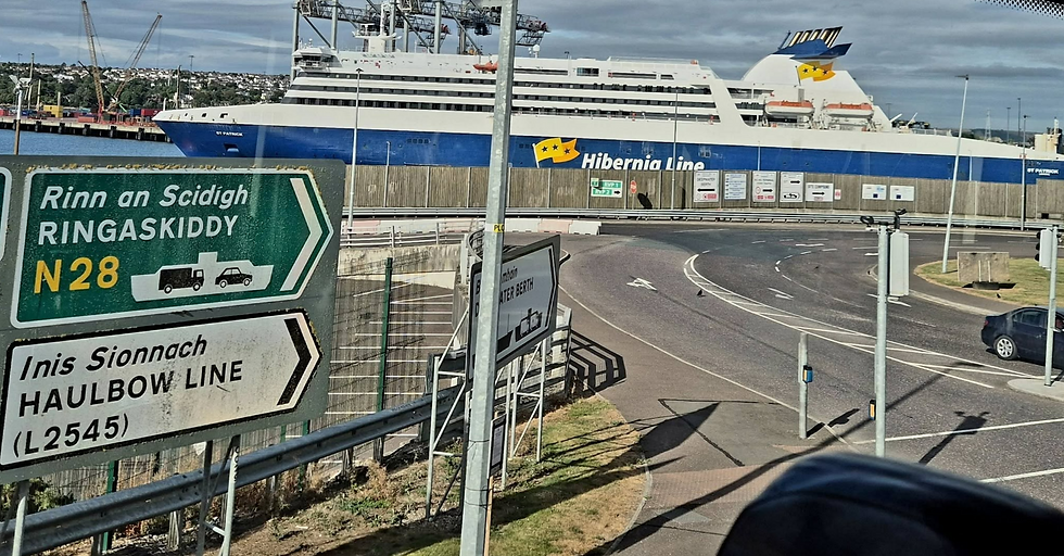 Road signs for Ringaskiddy and Haulbowline in foreground, with a large Hibernia Line ferry docked at Cork harbour behind.