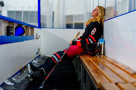 Hockey Player sitting at end of bench looking up with stick.