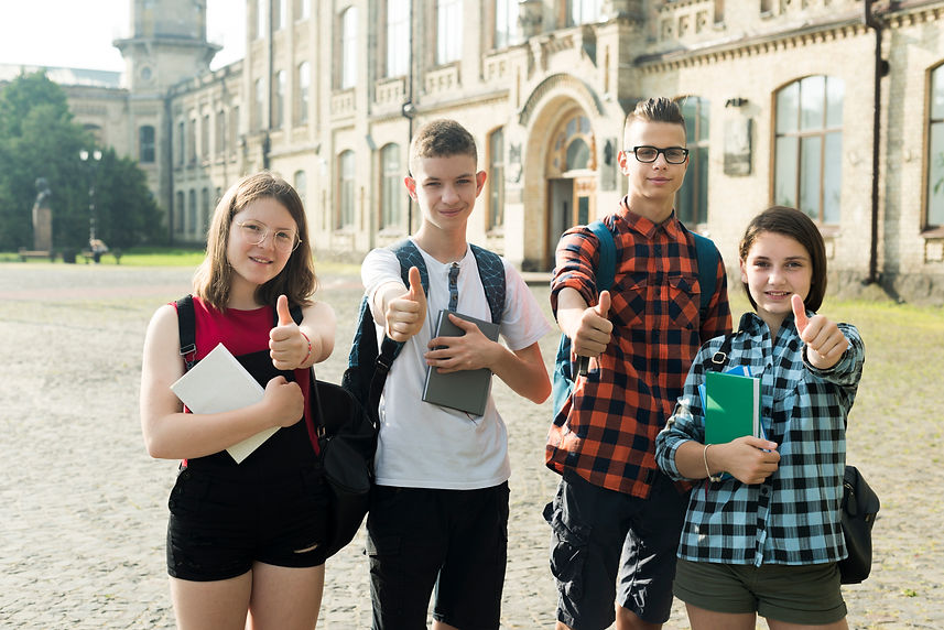 Four teenage students standing in front a college showing thumbs up
