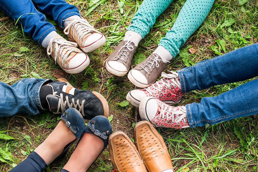 A Group Of Friends Sitting On The Green Grass Make Foot Circle With Their Legs Adn Different Shoes..