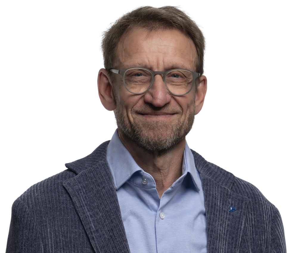 Studio portrait of a middle-aged man wearing glasses and a blazer. He has a friendly, professional demeanor against a black background.