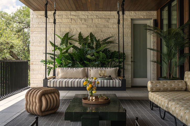 Covered Austin terrace with built-in seating, striped cushions, tropical plants and tile and stone coffee tables.
