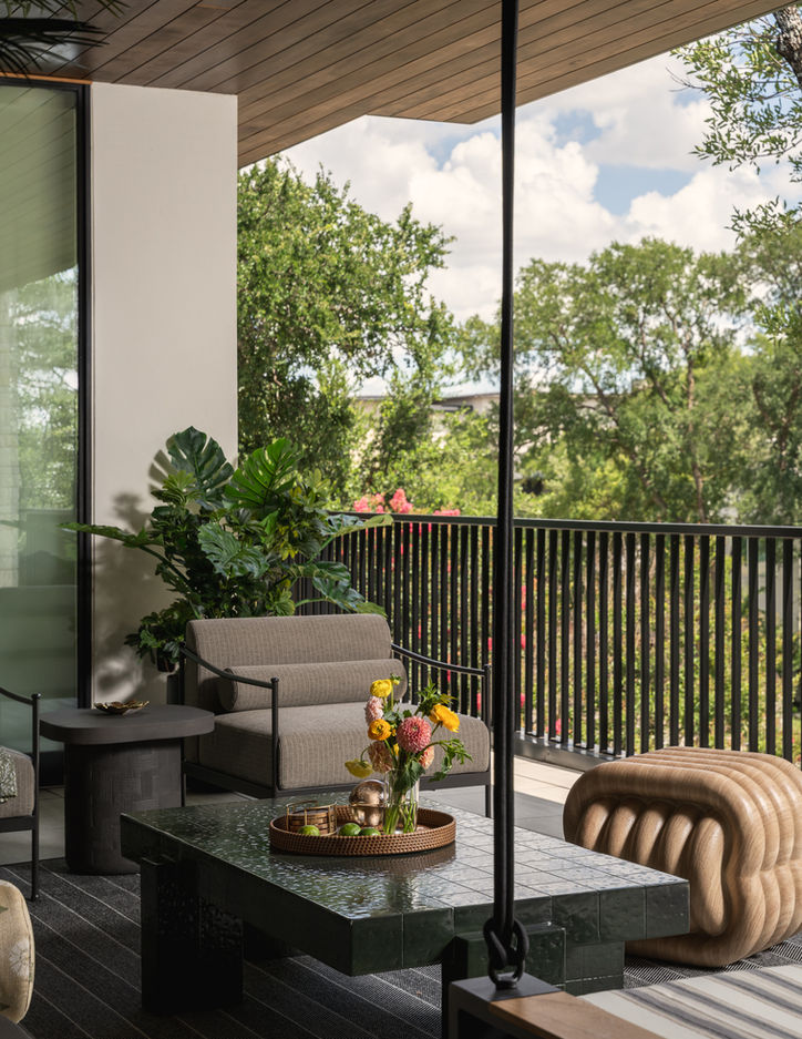 Open-air Austin balcony surrounded by trees with sculptural furniture and layered neutral upholstery.