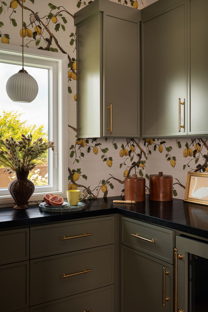 Custom green pantry cabinetry with botanical Wallshoppe grasscloth and black stone countertops.