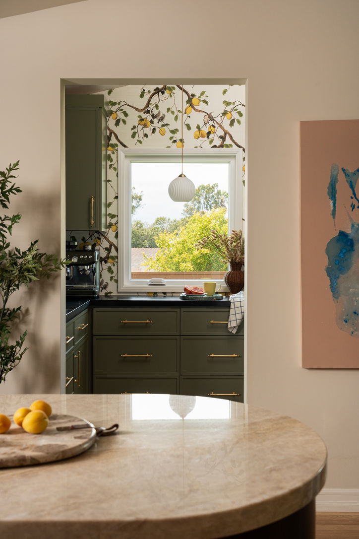 View into a green pantry with botanical grasscloth wallpaper from the Taj Mahal quartzite kitchen island.