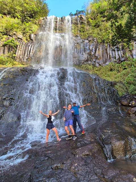 Three people posing at the base of a powerful waterfall