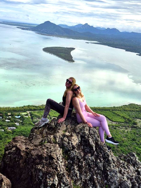Two women on rocky cliff viewing a bay and mountains