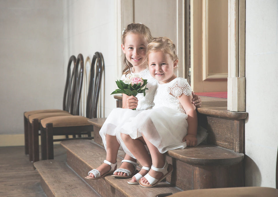Twee bloemenmeisjes in witte jurkjes met bloemetjes, zittend op een houten trapje
