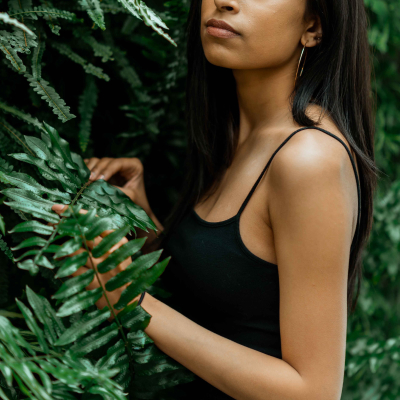 Young woman in a black tank top touching lush green fern leaves