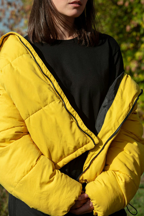 Person wearing a yellow puffer jacket over a black top