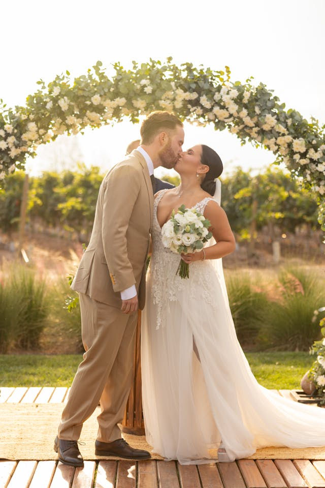 Newlyweds kissing under a white floral wedding arch