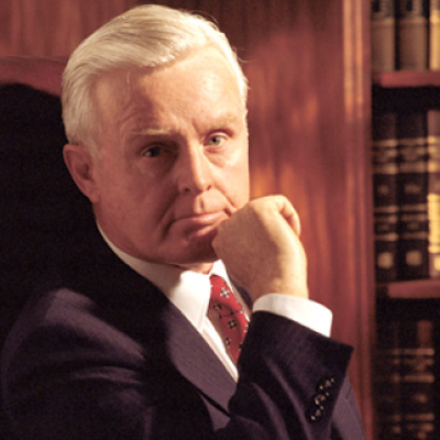 Man with white hair, suit, hand on chin, thoughtful