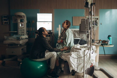 Partner supporting a laboring woman beside the hospital bed while she leans back during a contraction
