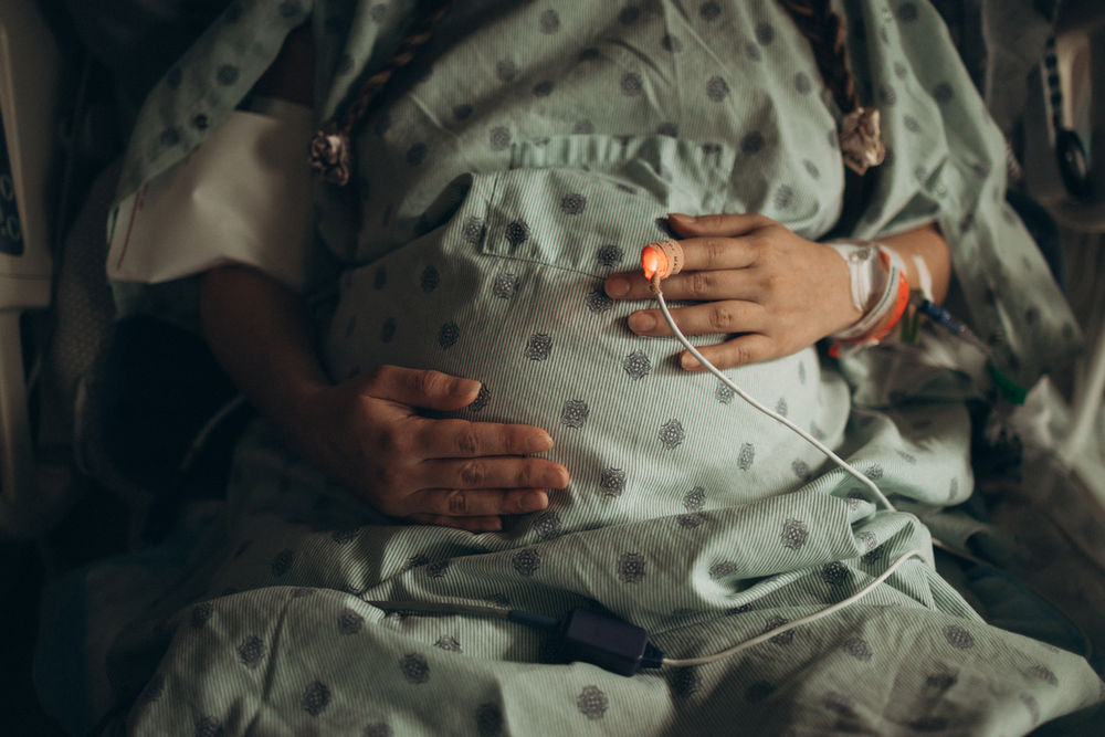 Close-up of a pregnant woman resting both hands on her belly while wearing a hospital gown during labor
