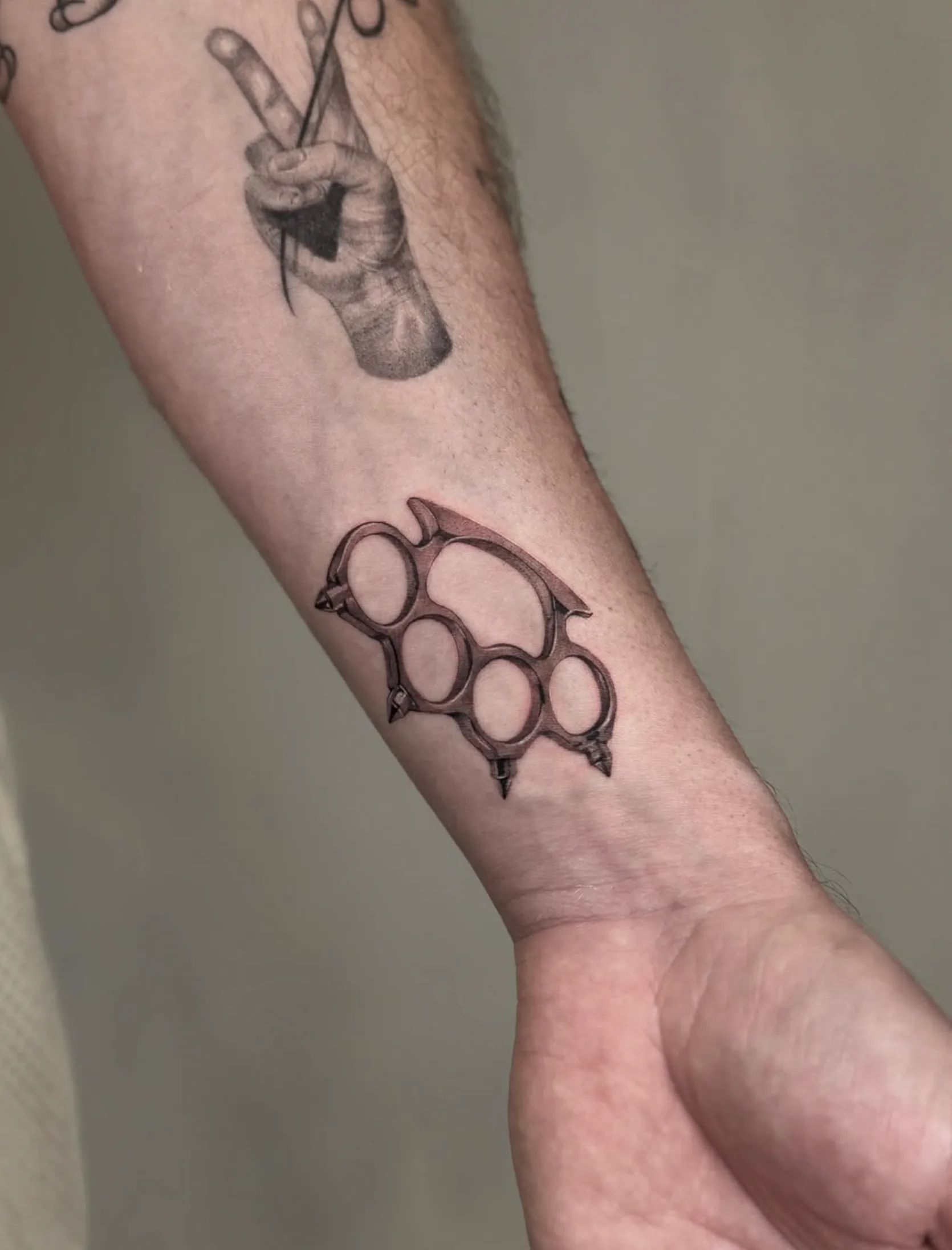Black and grey brass knuckles wrist tattoo by Tasos at The Story of Us MCR, near Deansgate Manchester
