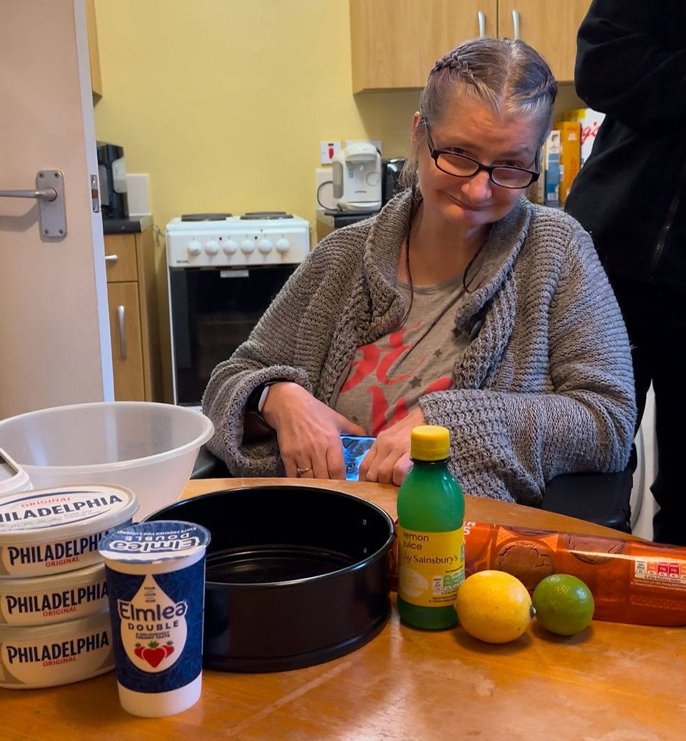 white woman.sitting down.on a wheelchair.in a kitchen.food on table.yellow wall.door in background.