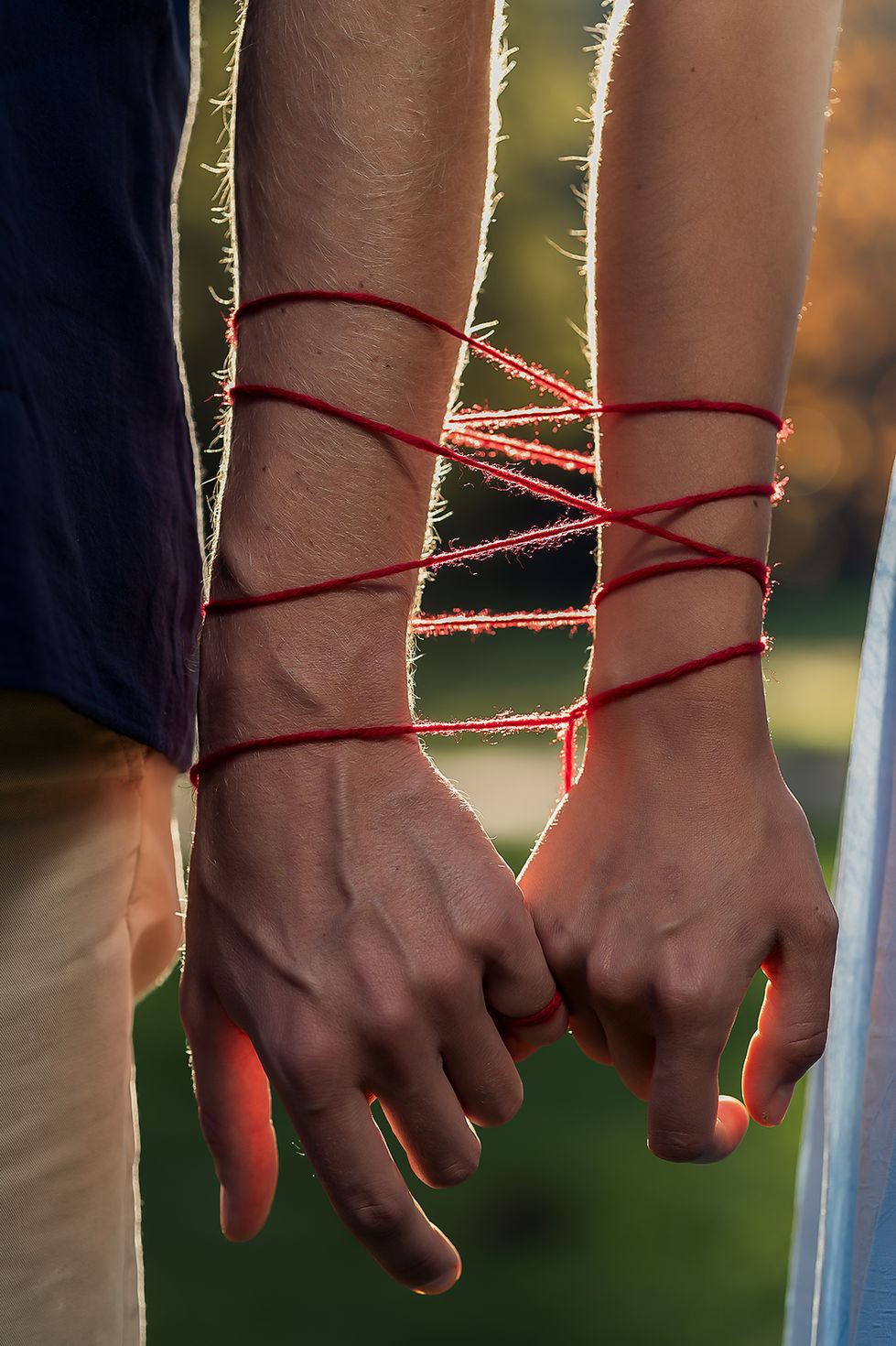 Twin Flame pár držiaci sa za ruky, okolo ktorých sa vinie červená niť osudu, zobrazujúca spletitý priebeh ich životnej cesty.